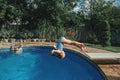 Brave athletic girl in swimsuit diving in pool from springboard. Child kid enjoying having fun in swimming pool on home backyard.