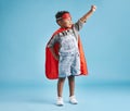 Brave cheerful boy in superhero cape and mask clenching his fist pretending to fly on blue background. Strong kid ready