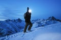 Brave explorer with headlamp and backpack and a snowboard behind his back climb on great snowy mountain at night. Traveler wearing