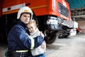 Brave firefighter in uniform holding little saved girl standing on black background