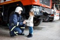 Brave firefighter in uniform holding little saved girl standing on black background