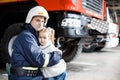 Brave firefighter in uniform holding little saved girl standing on black background