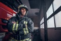 Fireman wearing protective uniform standing next to a fire engine in a garage of a fire department, crossed arms and Royalty Free Stock Photo