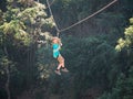 Brave little boy in helmet and harness zip lining at adventure park