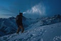 Brave man with headlamp, backpack and a snowboard behind his back climb night on snowy mountain. Man commit ski tour in high ridge Royalty Free Stock Photo