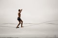 Brave man walking on a slackline against the grey sky