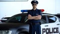 Brave police officer in service cap and sunglasses posing into camera near car Royalty Free Stock Photo