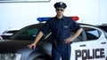 Brave policeman in service car and sunglasses posing on camera near patrol car