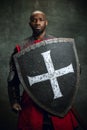 Portrait of medieval warrior, dark skinned bald knight with dirty wounded face holding shield and sword isolated over Royalty Free Stock Photo