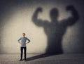 Brave teenager boy facing his fears as a powerful hero. Guy casting a strong muscular bodybuilder shadow, showing big biceps. Self Royalty Free Stock Photo