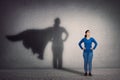 Brave woman keeps arms on hips, smiling confident, casting a superhero with cape shadow on the wall. Ambition and business success Royalty Free Stock Photo