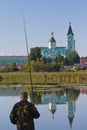 Fisherman`s figure with a fishing rod on a bank of river Riv with Trinity convent of russian orthodox church