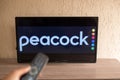 Brazil, Rio de Janeiro - May 19, 2023: a close-up of a hand holding a TV remote control seen in front of the Peacock logo