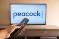 Brazil, Rio de Janeiro - May 19, 2023: a close-up of a hand holding a TV remote control seen in front of the Peacock logo