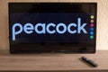 Brazil, Rio de Janeiro - May 19, 2023: a close-up of a hand holding a TV remote control seen in front of the Peacock logo