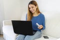 Brazilian beautiful girl doing shopping online with credit card and laptop while sitting on sofa at home Royalty Free Stock Photo