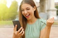 Brazilian exuberant business woman cheering at good news on her mobile phone and punching the air with her fist