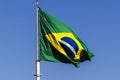 Brazilian flag flutters on a flagpole with the blue sky