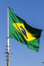 Brazilian flag flutters on a flagpole with the blue sky