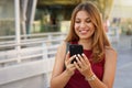 Brazilian girl using smartphone outdoor. Cheerful young woman chatting with mobile phone near train station Royalty Free Stock Photo