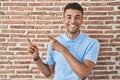Brazilian young man standing over brick wall smiling and looking at the camera pointing with two hands and fingers to the side Royalty Free Stock Photo