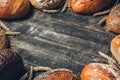 Bread border on wood background with copy space. Black, brown and white whole grain loaves with spikelets. Different