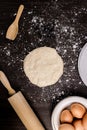 Bread concept a bun dough, a petite wooden spatula, a rolling pin, and a bowl of a few eggs organized on the dark wooden table