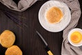 Bread concept buns, a dish of flour, a knife, and a tiny bowl of raw egg lying on the dark wooden table