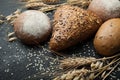 Bread of different kinds on a dark board with spikelets of wheat, rye and oats. Carbohydrates and diet