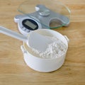 Bread flour in white bowl with rubber scraper and scale on wood