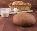 Round bread and a glass of milk on a wooden table and a basket of bread and eggs on a napkin