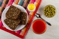 Bread with sunflower seeds in plate, salt shaker on napkin, glass with tomato juice, bowl with green peas, spoon on wooden table. Royalty Free Stock Photo