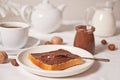 Bread toast with chocolate cream butter, jar of chocolate cream, cuop of tea, jar of milk, teapot on the white background