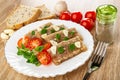 Bread, tomato cherry, white plate with pieces of meat jelly, garlic, basil, tomato, pepper shaker, fork on wooden table