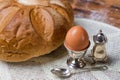 Bread on the wooden table and serviette, egg in silver utensil