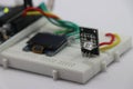 Breadboard circuit using OLED module,Pulse sensor and some wires connected to microcontroller on the background shows the concept