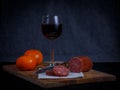 Breadboard with a sliced meat saucage a glass of red wine and two mandarins