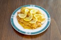 Breaded chicken fillets soaked in Chinese lemon sauce on white plate and brown wooden table