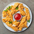 Breaded chicken strips with tomato ketchup on a white plate. Fast food on dark brown background. Top view Royalty Free Stock Photo