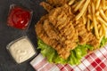 Breaded chicken strips with two kinds of sauces and fried potatoes on a stone background. Fast food on black stone Royalty Free Stock Photo