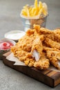 Breaded chicken strips with two kinds of sauces and fried potatoes on a wooden Board. Fast food on dark brown background Royalty Free Stock Photo