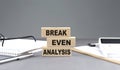 BREAK-EVEN ANALYSIS text on wooden block with notebook,chart and calculator, grey background Royalty Free Stock Photo