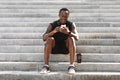 Break In Training. Athlete Black Guy Resting On Steps With Smartphone