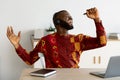 Break In Work. Cheerful African Guy In Traditional Shirt Singing At Workplace Royalty Free Stock Photo