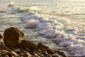 Breakaing wave with patel sunlit foam and backwash, crawling toward rocky shore Royalty Free Stock Photo