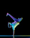 Breakdancer. Young flexible athletic man dancing breakdance freezes in sport outfit against black background in neon Royalty Free Stock Photo