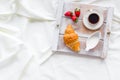 Breakfast in bed with croissant, coffee in cup with milk on tray on white bed background top view Royalty Free Stock Photo