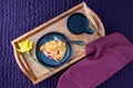 Breakfast in bed, homemade cranberry scone on black plate and wood tray on a purple bedspread