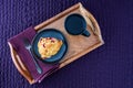 Breakfast in bed, homemade cranberry scone on black plate and wood tray on a purple bedspread