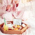 Breakfast in bed with I love you text on lighted box, coffee, macaroons on wooden tray and blurred cropped woman in a bathrobe